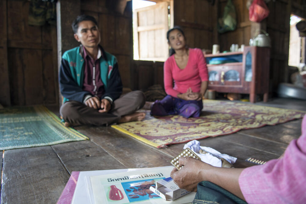 A couple sitting on the floor and a health professional teaching them about contraceptive methods and medicine