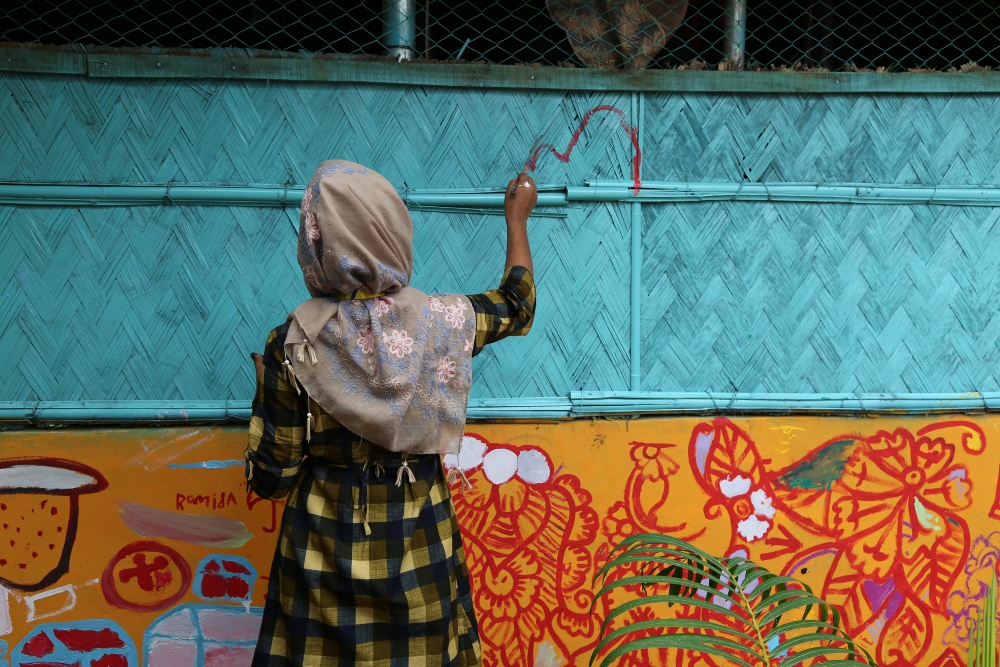 Girl wearing a head scarf, facing a colorful wooden wall and drawing on it