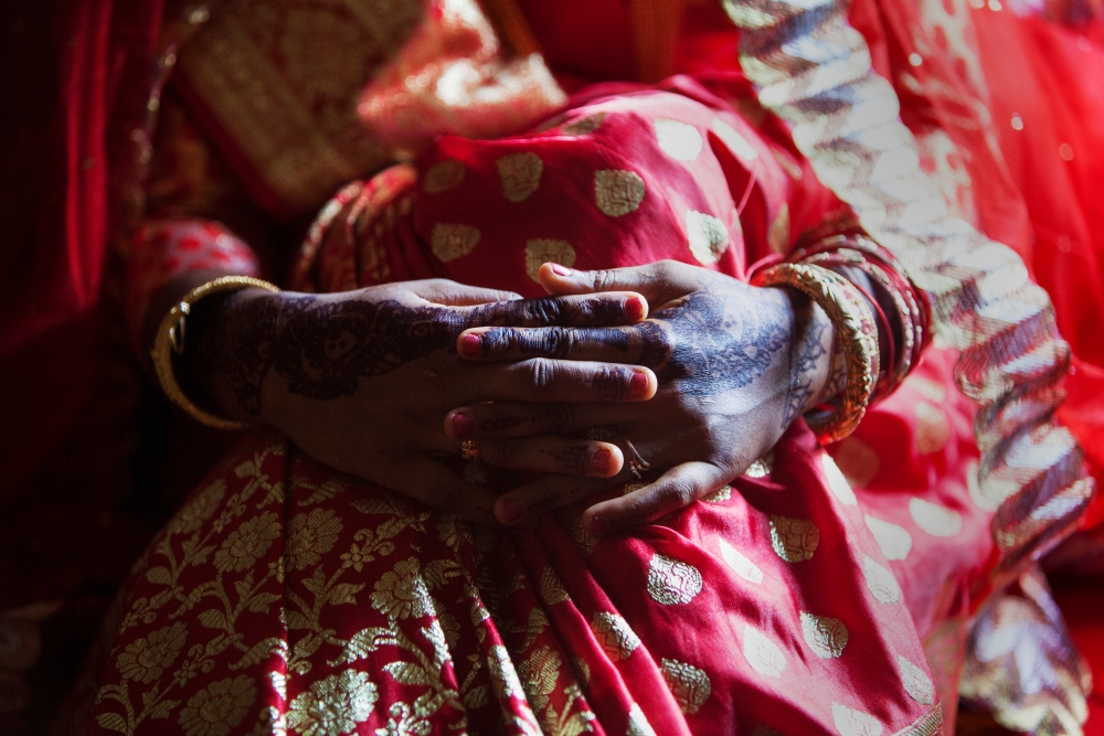 Close-up of a woman's hands holding her own knees, she is wearing traditional clothes and has her hands painted