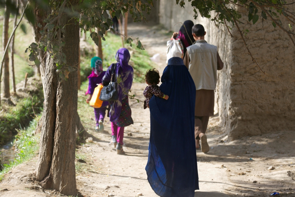 People walking in a rural and dry area, they seem to be a family and are wearing traditional clothes