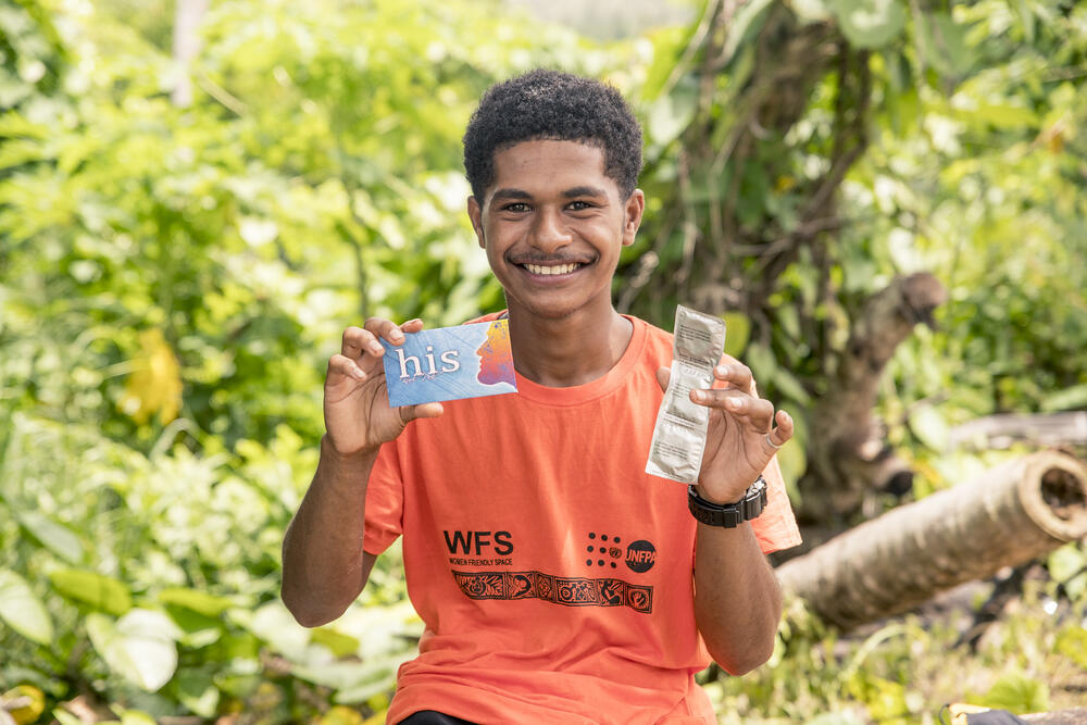 Young man wearing a uniform written "Women Friendly Spaces" and the UNFPA logo, he is holding condoms and a card