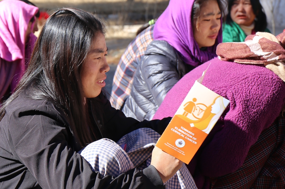 Woman sitting on the grass reading a brochure that says "Towards elimination of cervical cancer"