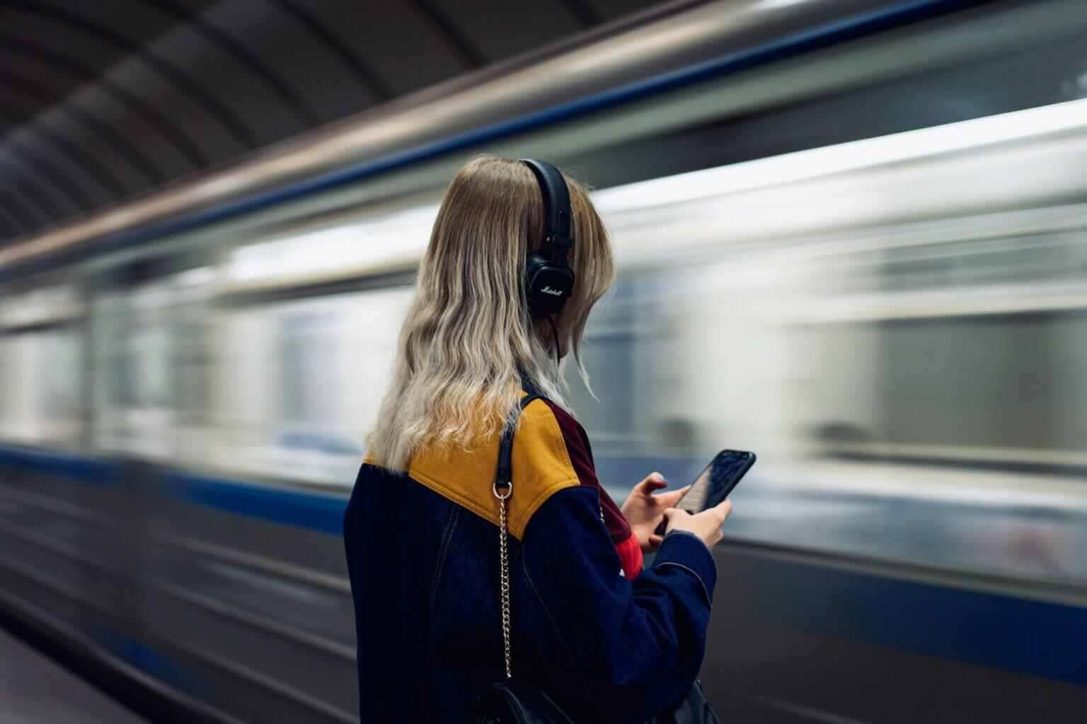 Woman at the subway holding her phone with headphones on