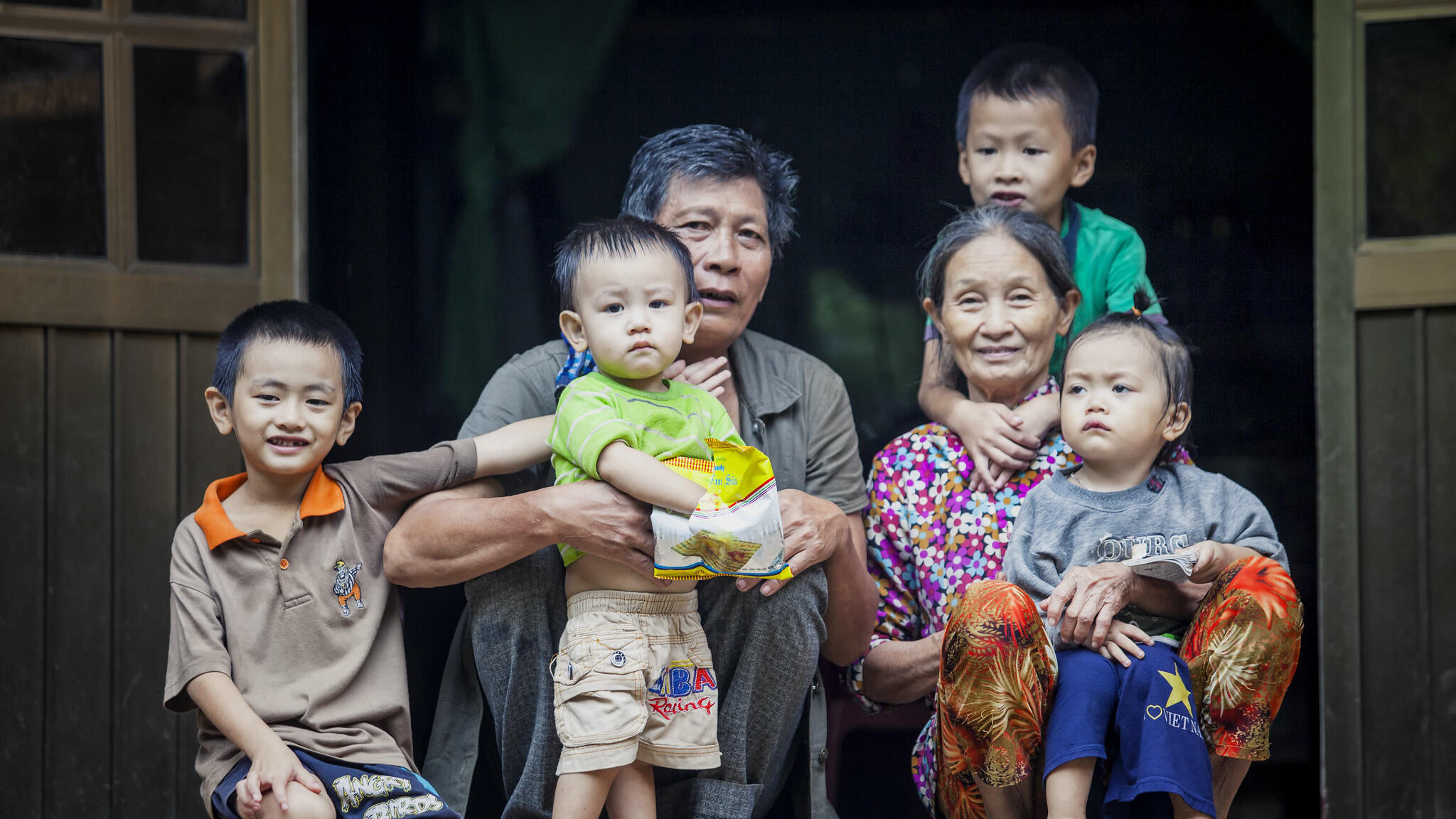 An older man and an older woman sitting at a doorstep with 4 young children