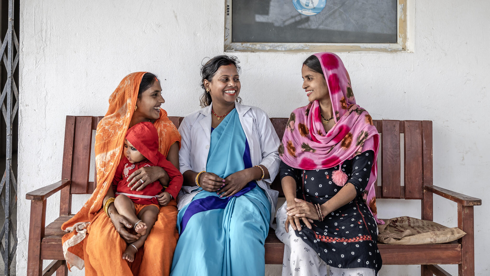 Three women sitting, chatting and smiling, one is holding a baby