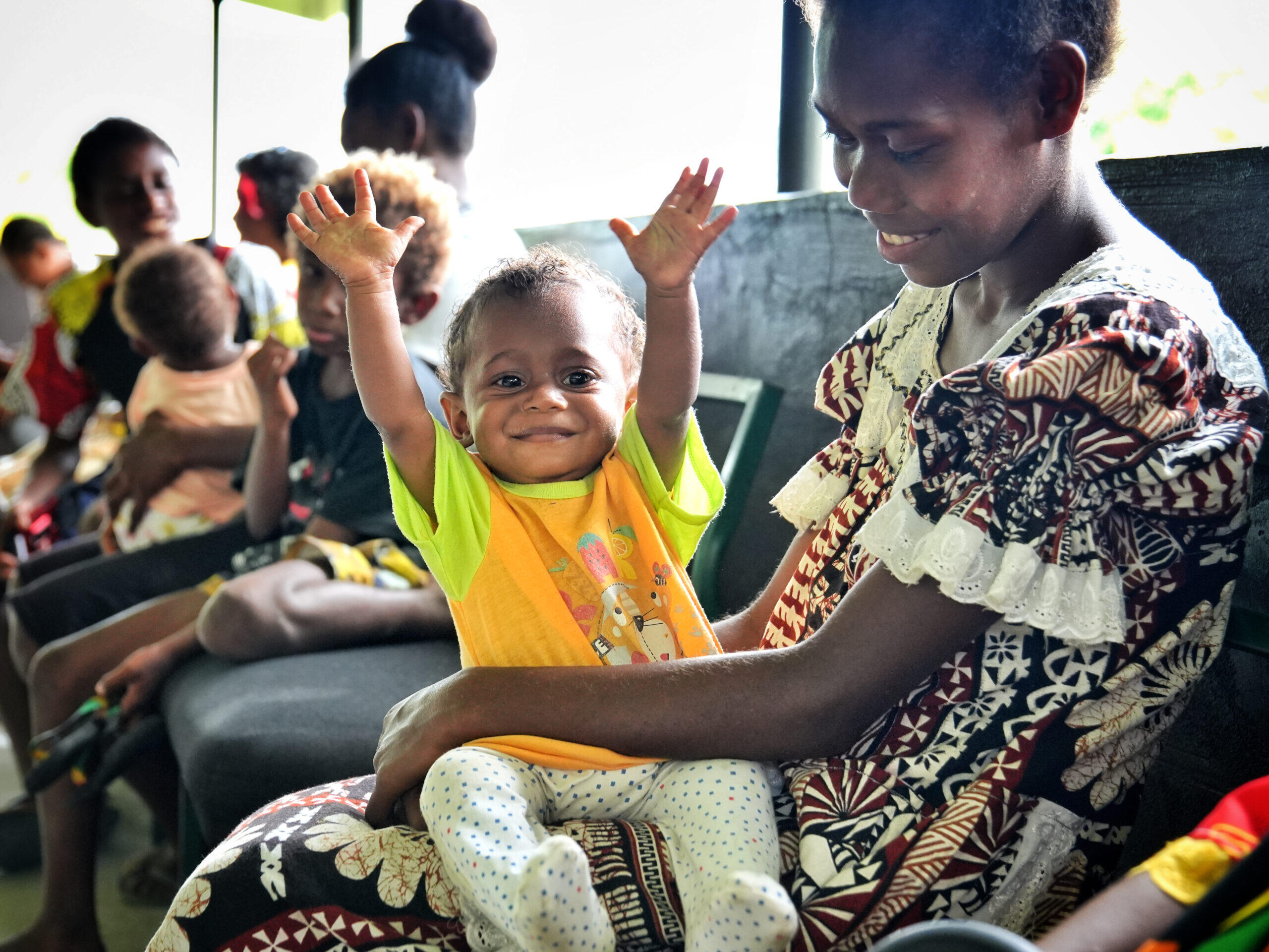 Woman from the pacific holding her child with the hands up, both are smiling