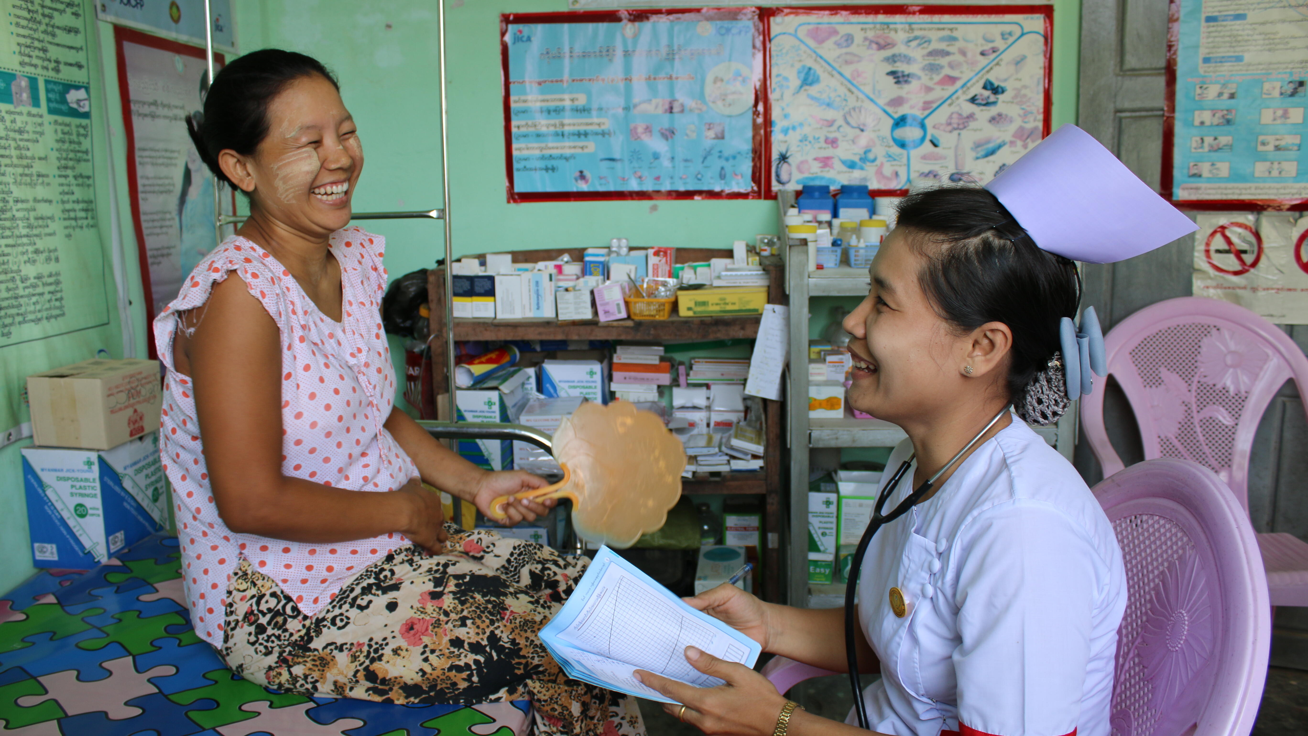 A pregnant woman and a midwife laughing together at a medical clinic in Myanmar