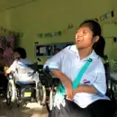Image of a disabled girl laughing in her wheelchair as her friend, also in a wheelchair, laughs with her in the background